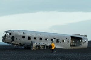 A person in a yellow raincoat approaching an old crashed airplane in a field