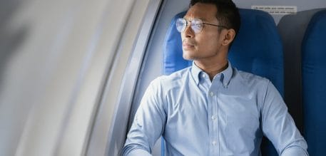 Tired asian man with headache feeling sick while sitting in the airplane.