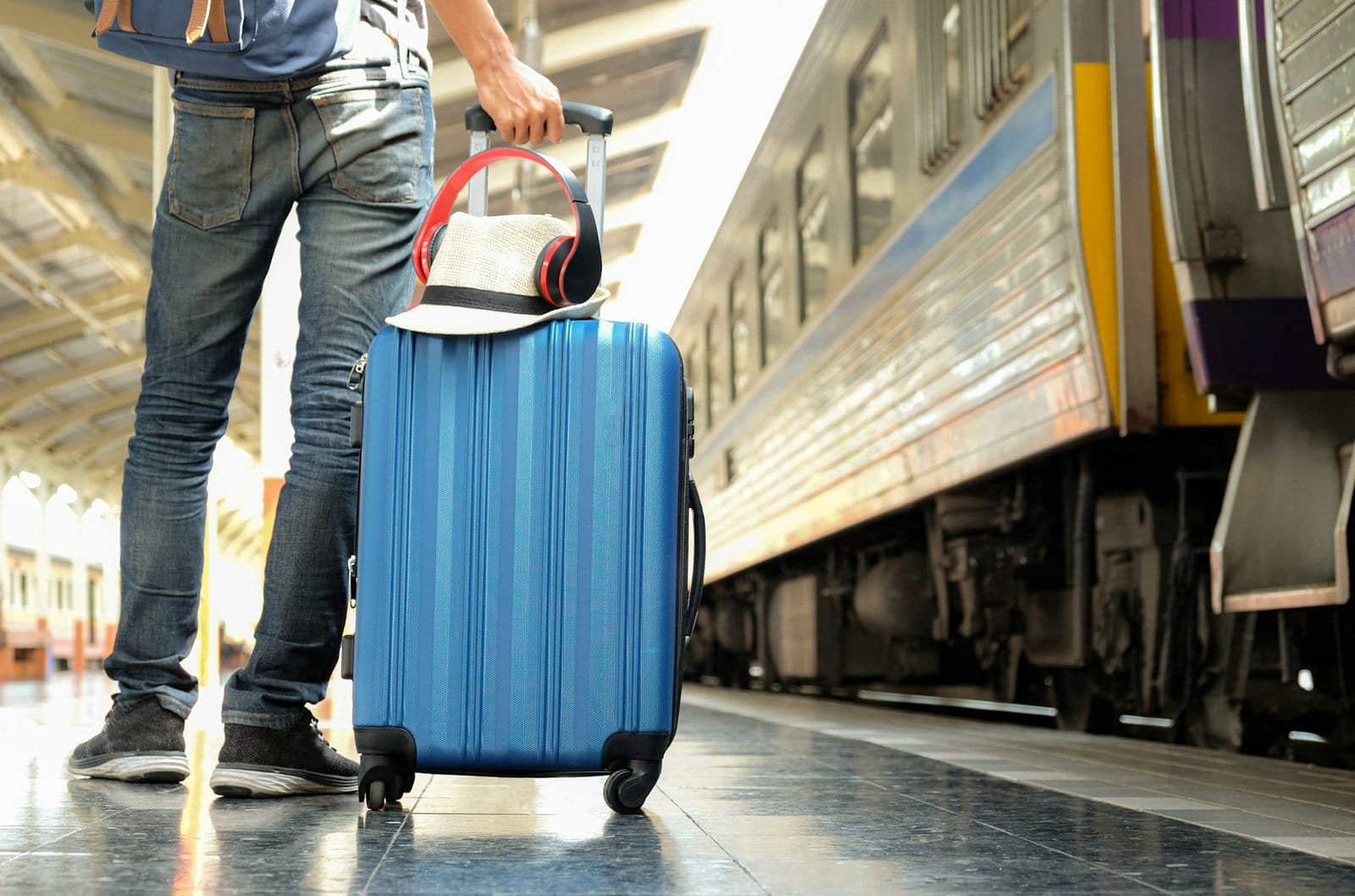 Traveler with a blue suitcase is waiting for the train.Hat and headphone placed on the suitcase.