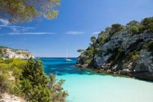 Coastal bay and distant view of yacht, Cala Macarelleta, Menorca, Spain