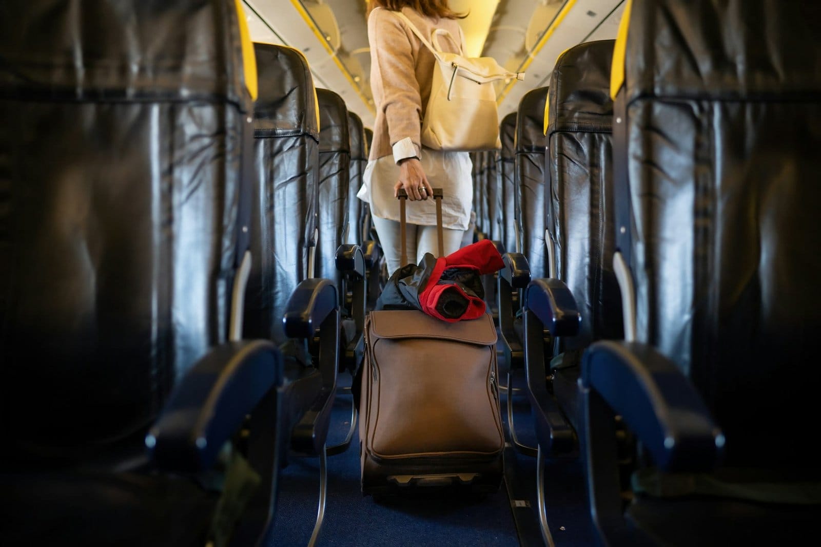 Crop female traveler walking with luggage on passage inside airplane