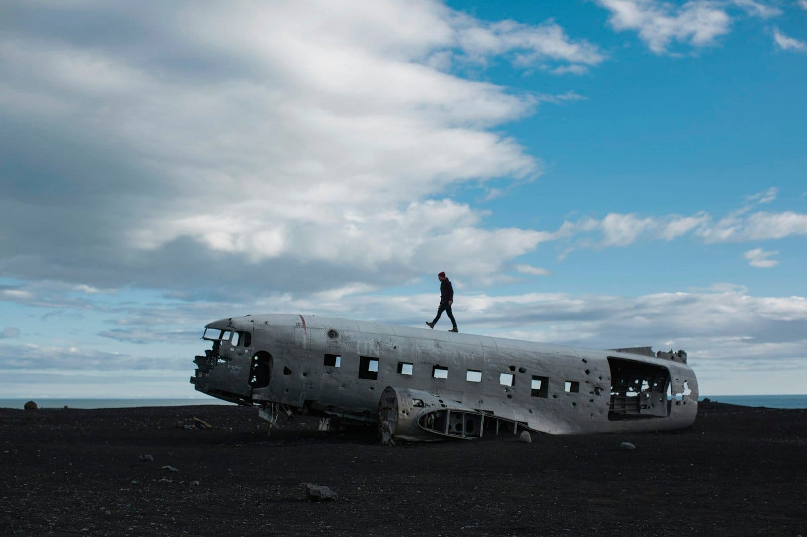 Person standing on a crashed airplane fuselage under cloudy skies.