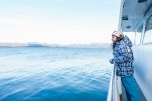 Girl leaning against railing on boat sailing toward coast, Ushuaia, Tierra del Fuego, Argentina