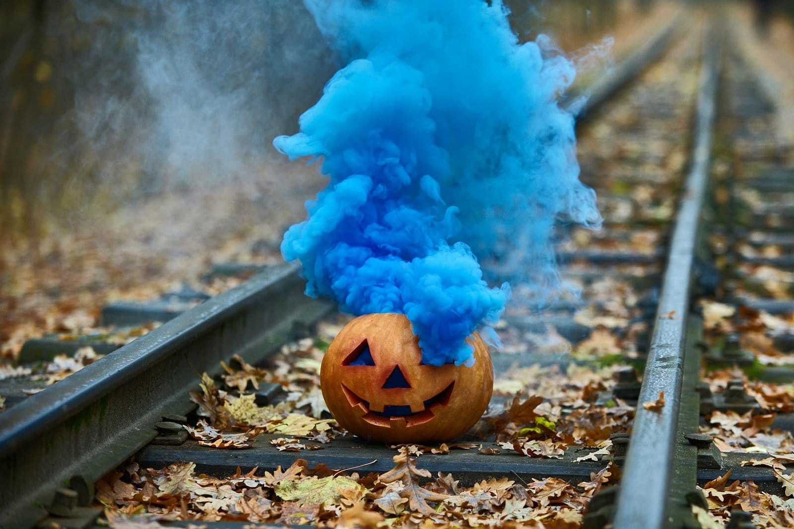 Smiling halloween pumpkin with bright blue smoke on the rails in the forest