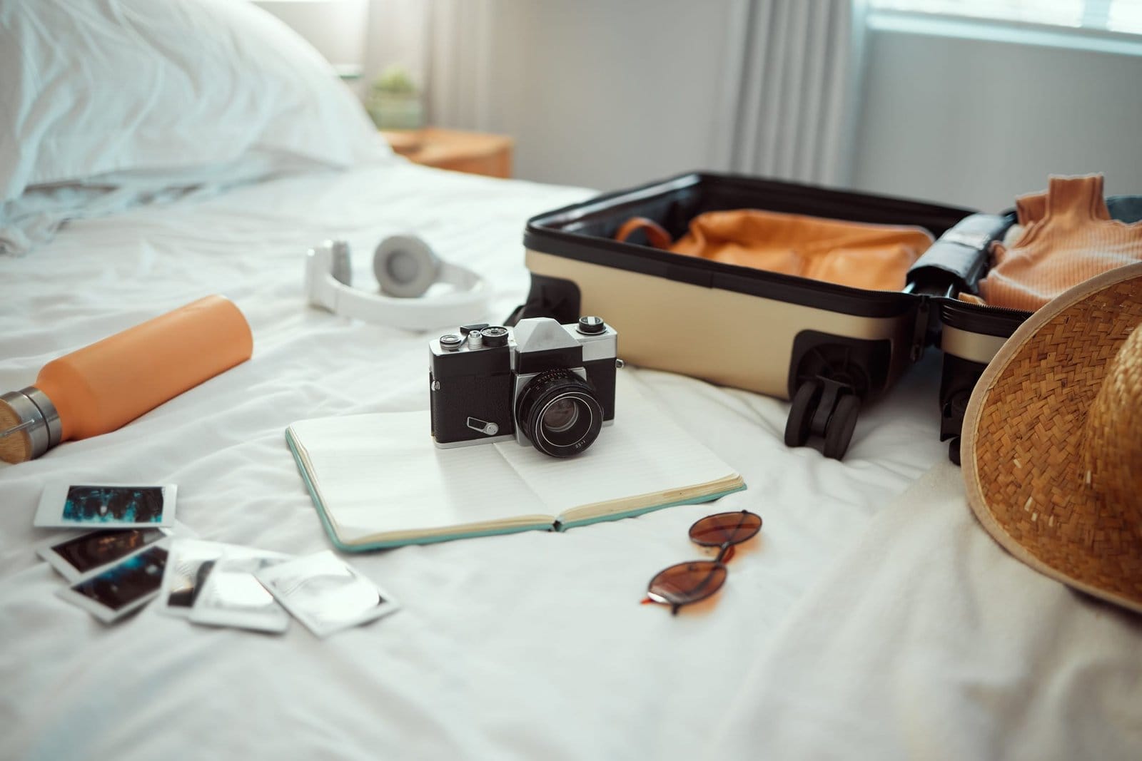 Hotel, travel and bedroom with a suitcase, camera and pictures on bed on holiday, vacation or trip.
