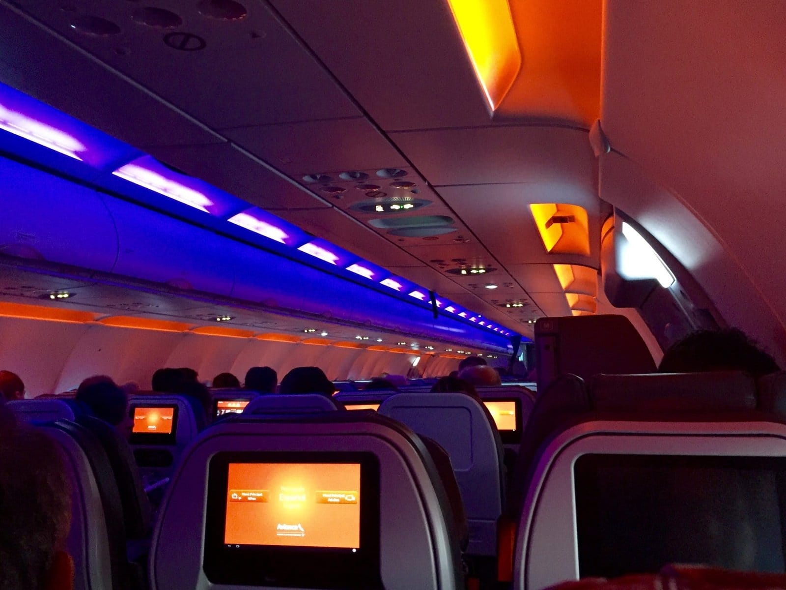 Interior of an airplane illuminated in orange and purple lights.