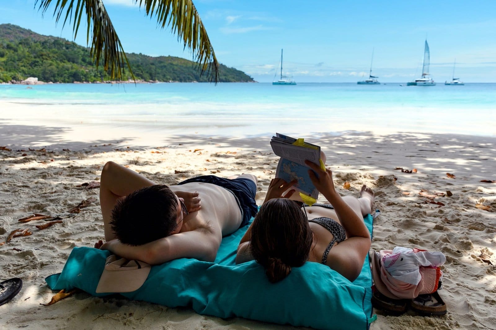 Young couple relaxing on beach and reading travel guide book.