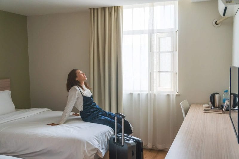 Young woman traveler with luggage sitting on the bed in hotel room