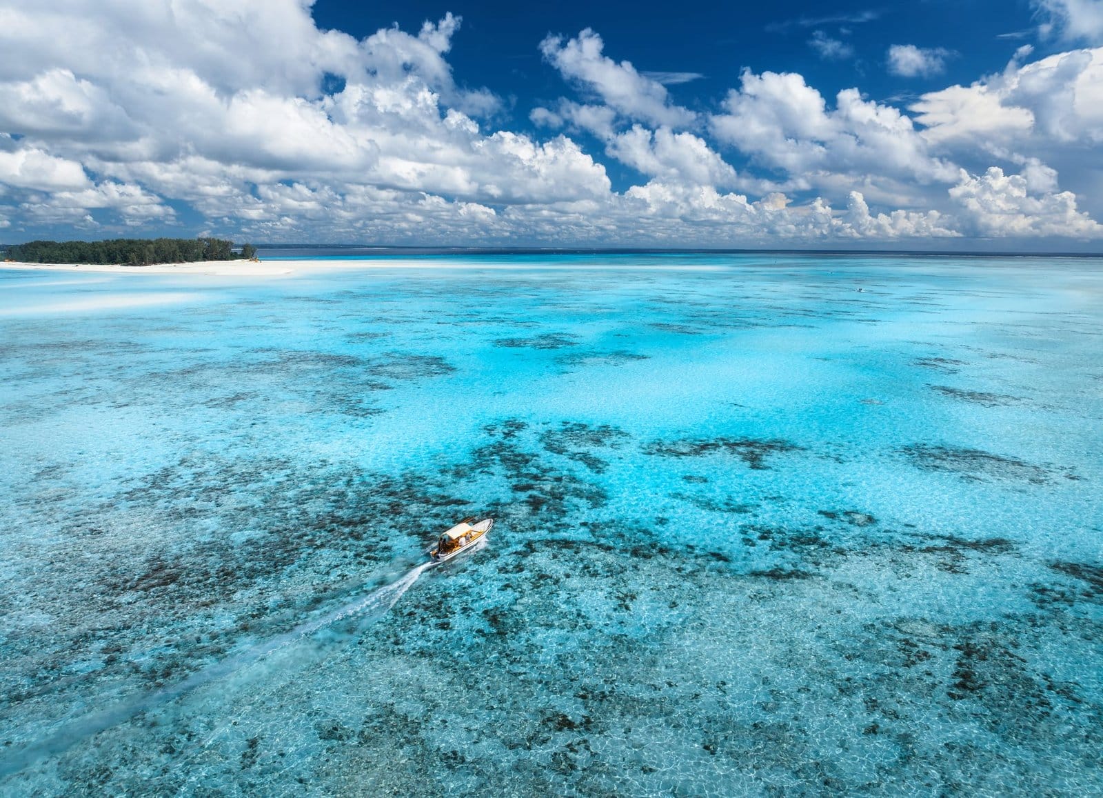 Aerial view of floating boat in clear azure water on summer day. Mnemba island, Zanzibar
