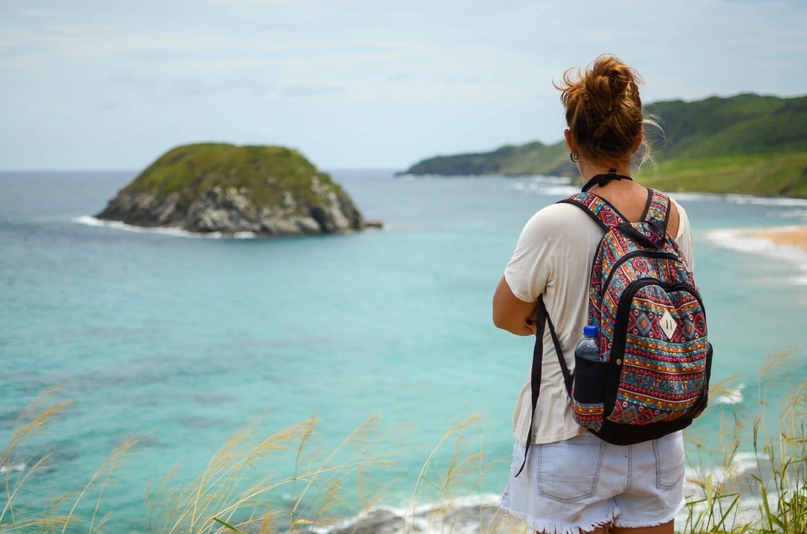 Blonde girl with a backpack looking at Lion Beach, Fernando de Noronha
