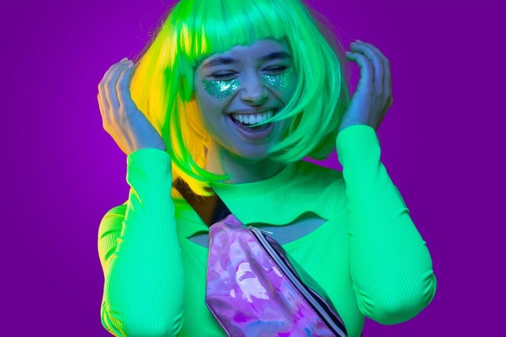 Funky girl wearing neon green top, belt bag, yellow wig and glitter on cheeks