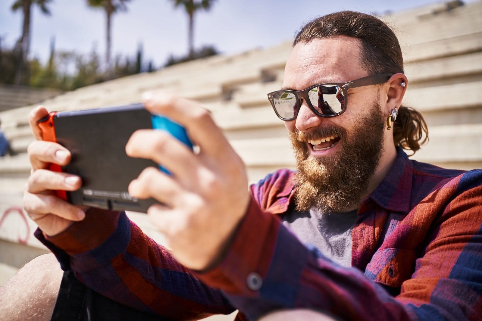 Joyful man smiling and having fun while playing video games with portable console outdoors.