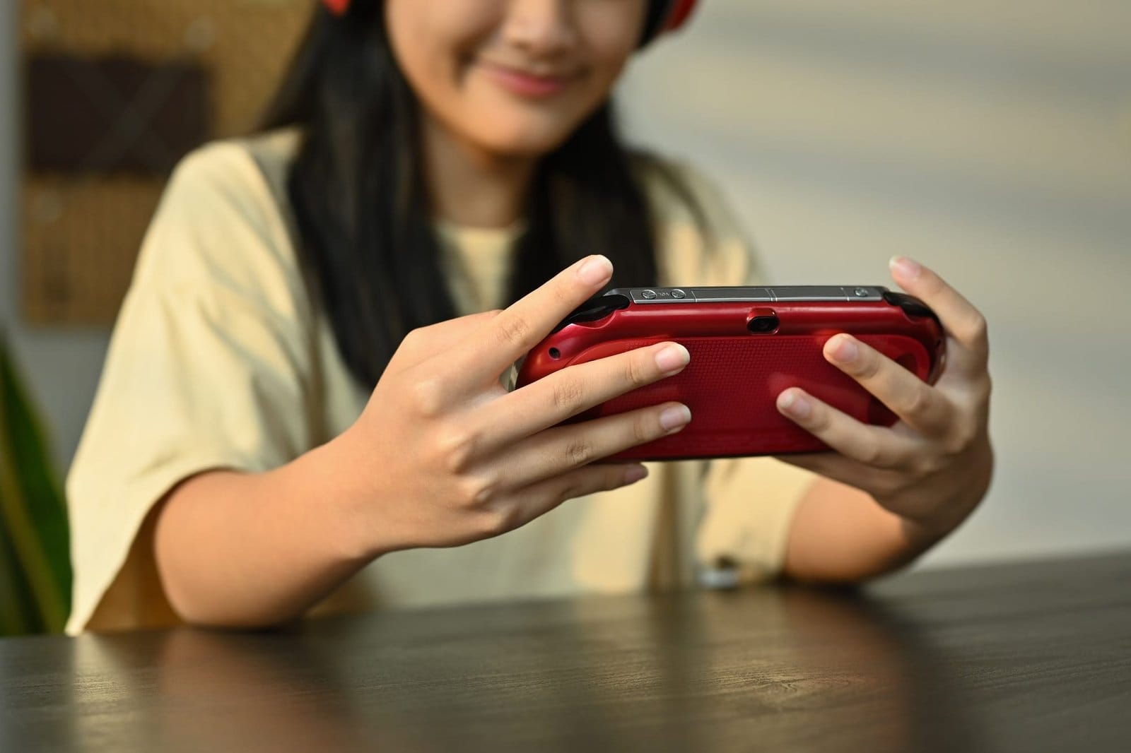 Smiling asian girl playing video game on a portable game console at home.