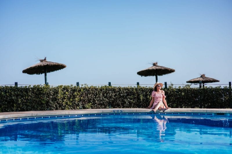 big long shot of a resort pool and a young woman sitting down and sunbathing big long shot of a resort pool and a young woman sitting down and sunbathing
